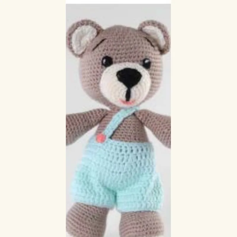 ⁨The same crocheted bear redesigned in blue dungarees, with cleaner finishing and brighter yarn⁩
