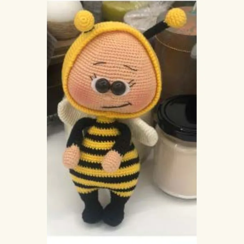 ⁨A crocheted doll in a bee costume with hard plastic eyes, photographed on a kitchen counter⁩