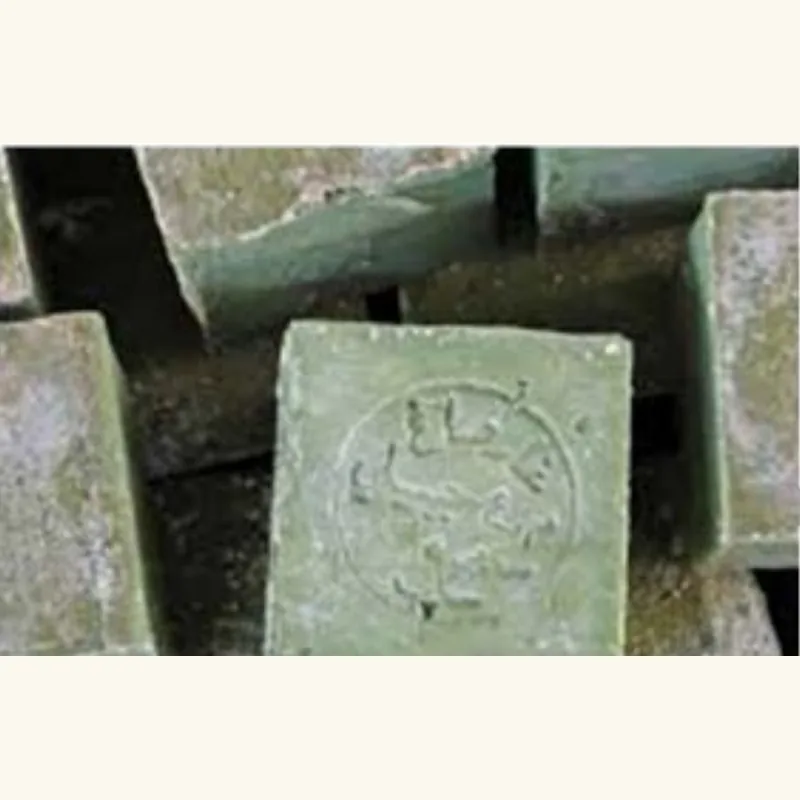 ⁨Rough unwrapped blocks of green Aleppo soap stacked on a workbench⁩